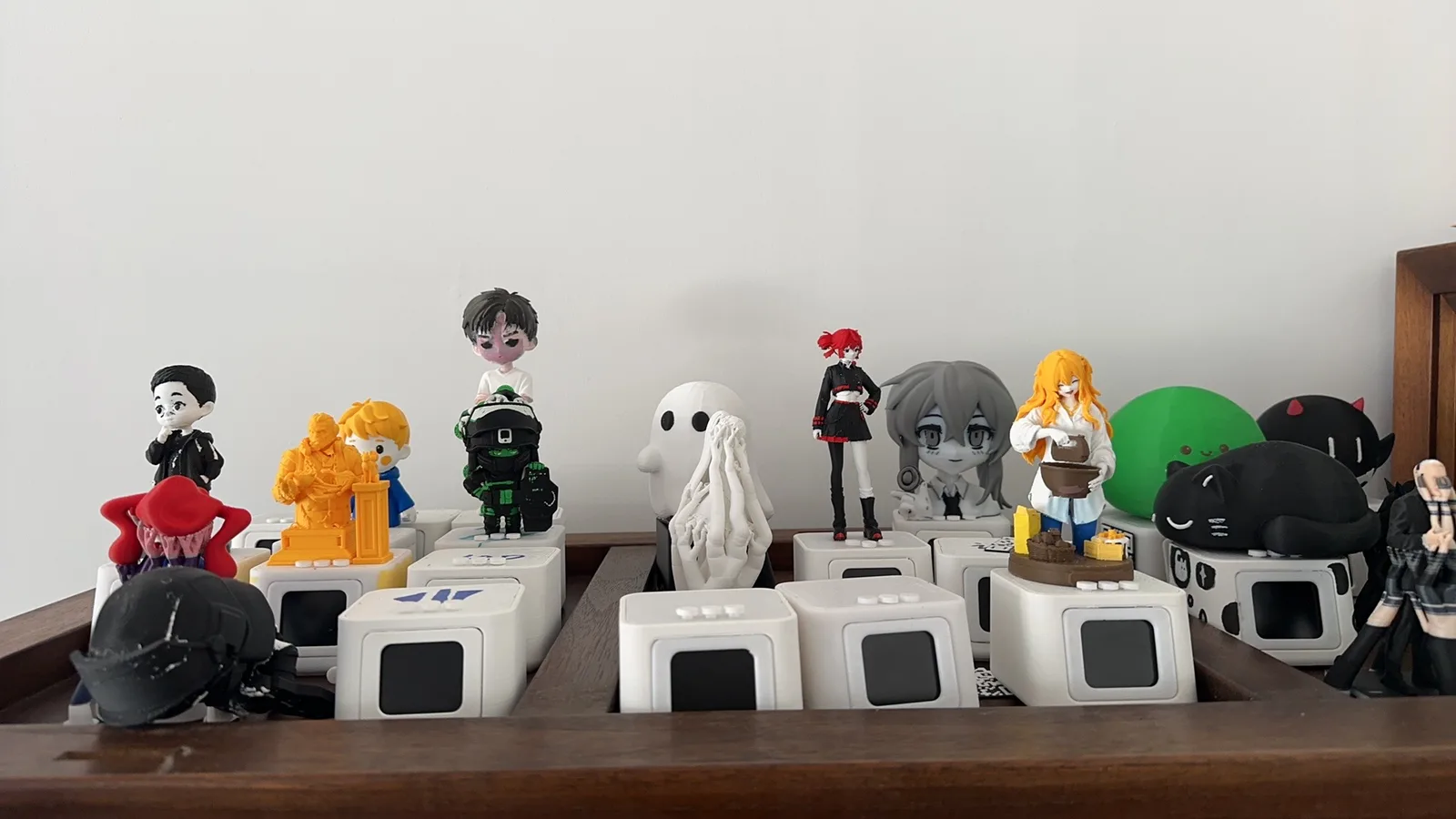 A wooden tray of small white devices with screens, each topped with a different 3D-printed figure