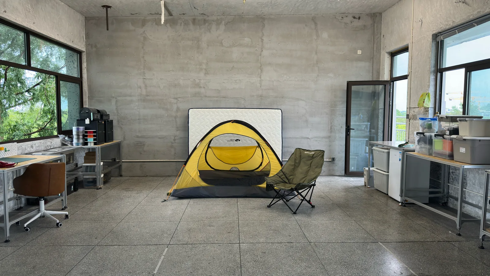 A yellow tent and a camping chair in the middle of a concrete classroom with workbenches along both walls