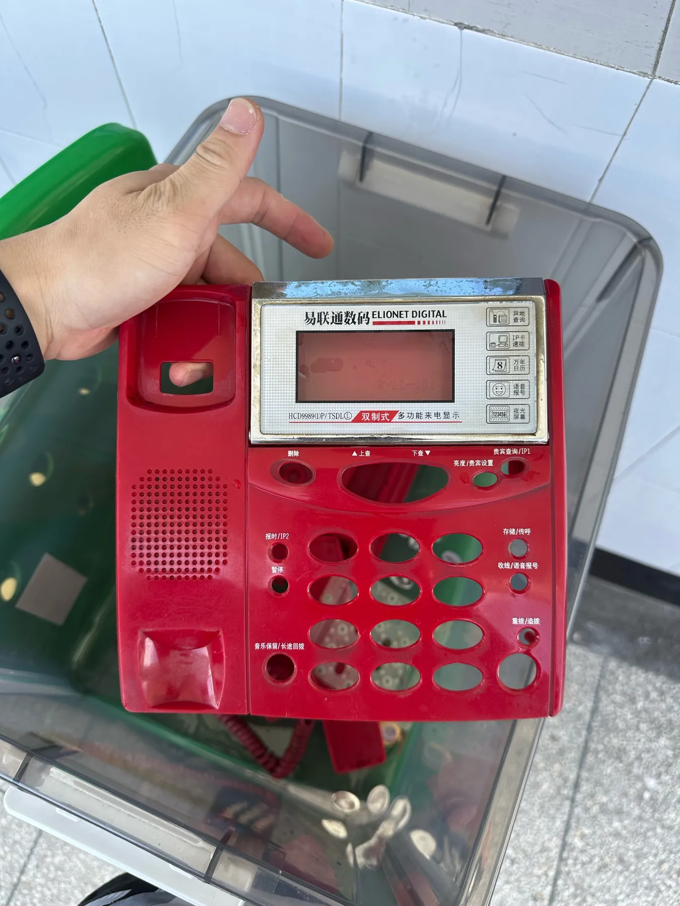 A hand holding the red faceplate of a keypad telephone with its keys removed
